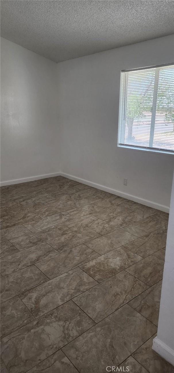 unfurnished room featuring a textured ceiling and baseboards