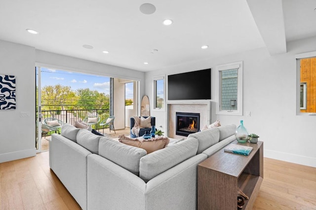living room featuring baseboards, a glass covered fireplace, recessed lighting, and light wood finished floors