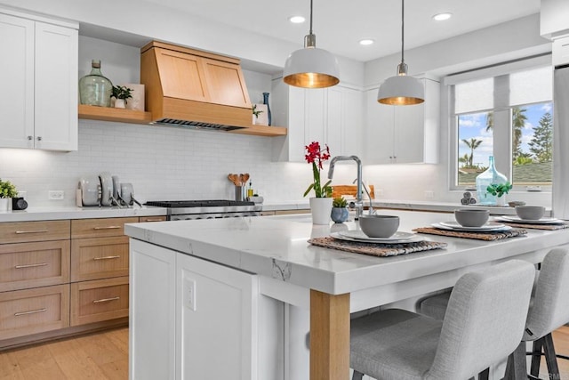 kitchen with open shelves, premium range hood, a center island with sink, decorative light fixtures, and a kitchen bar