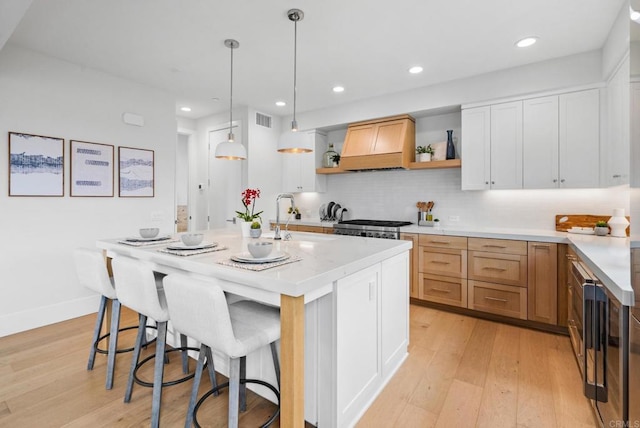 kitchen with open shelves, custom exhaust hood, light wood-type flooring, light countertops, and recessed lighting