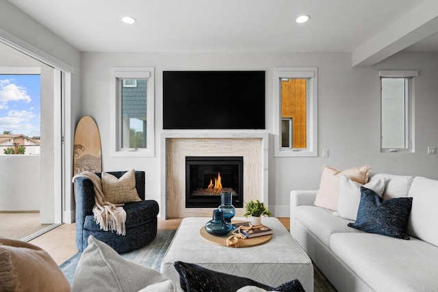 living room featuring recessed lighting, light wood-style floors, a glass covered fireplace, and baseboards