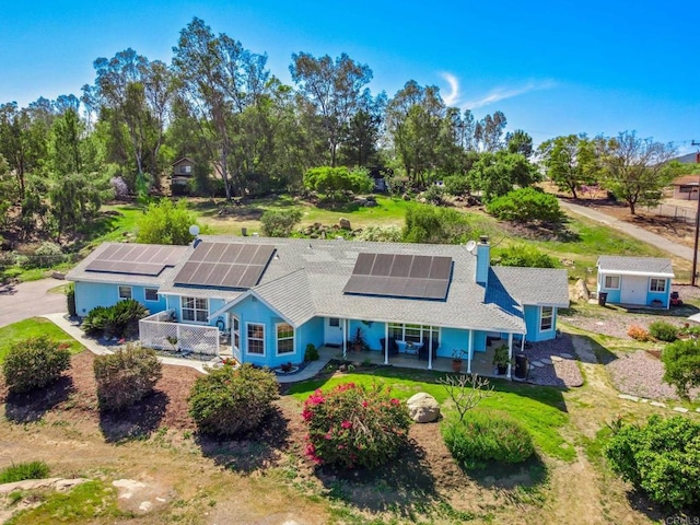 rear view of property with an outbuilding, a chimney, a patio, and roof mounted solar panels