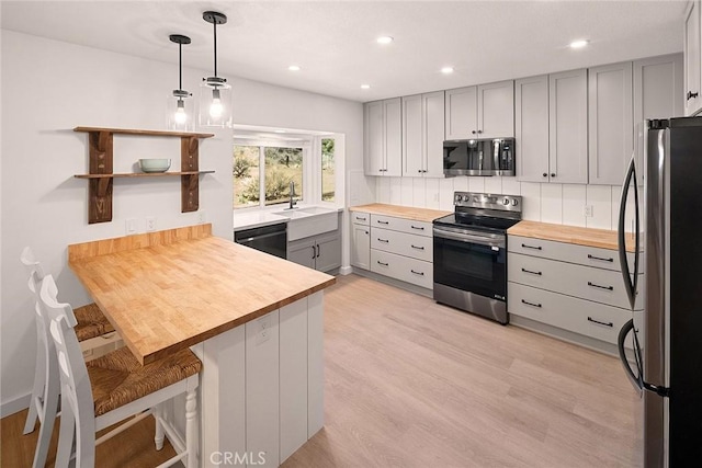 kitchen featuring a sink, appliances with stainless steel finishes, gray cabinetry, wooden counters, and a peninsula