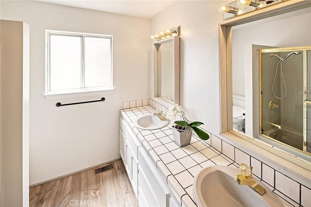 full bathroom with wood finished floors, a shower with shower door, toilet, and a sink