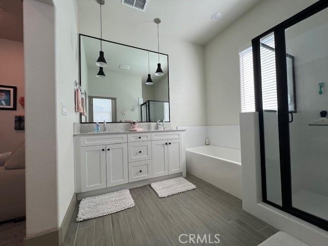 full bathroom with double vanity, a stall shower, visible vents, a garden tub, and wood finished floors