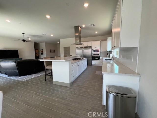 kitchen with exhaust hood, white cabinets, a center island, open floor plan, and built in appliances