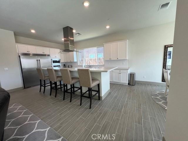 kitchen featuring stainless steel appliances, island range hood, light wood-style flooring, and white cabinetry