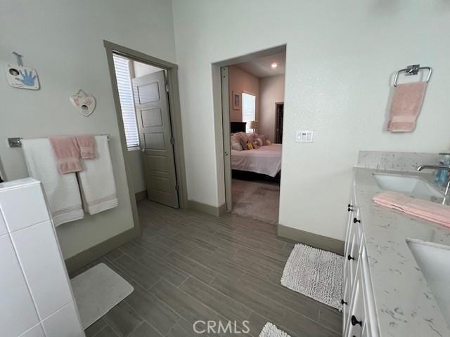 ensuite bathroom featuring wood finished floors, vanity, baseboards, and connected bathroom
