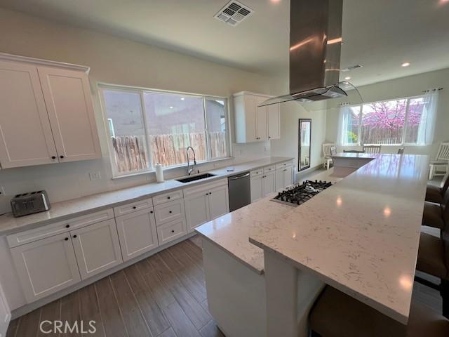 kitchen featuring visible vents, a sink, a kitchen bar, dishwashing machine, and island exhaust hood