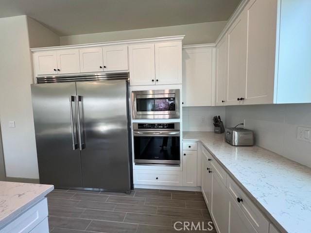 kitchen with wood tiled floor, light stone counters, built in appliances, and white cabinets