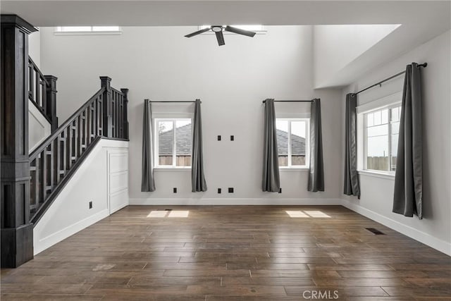 unfurnished living room with visible vents, baseboards, dark wood-style flooring, a ceiling fan, and stairway