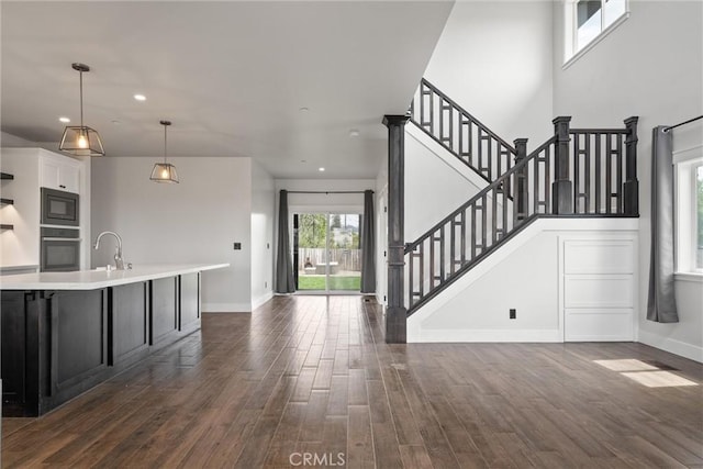 unfurnished living room featuring dark wood-style flooring, baseboards, recessed lighting, stairway, and a sink