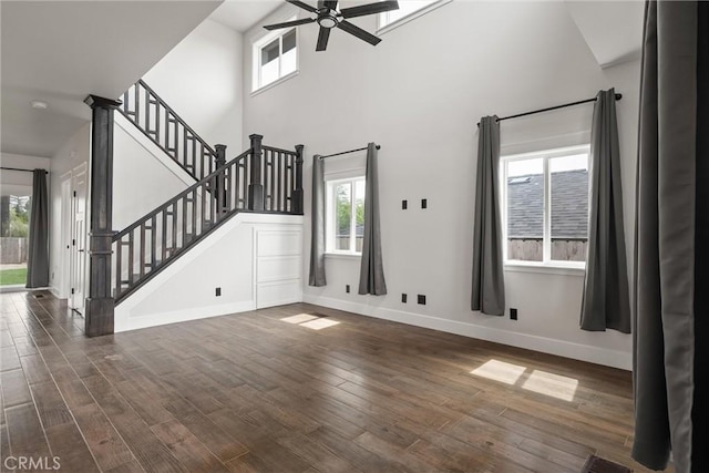 unfurnished living room with a towering ceiling, baseboards, dark wood-style floors, stairs, and ceiling fan