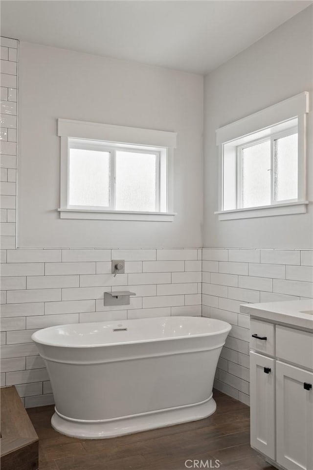 full bath with a soaking tub, a wealth of natural light, vanity, and wood finished floors