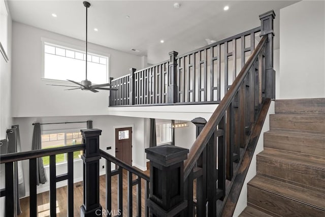 stairs featuring a wealth of natural light, ceiling fan, a high ceiling, and wood finished floors