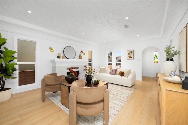living room featuring recessed lighting, light wood-style flooring, a textured ceiling, visible vents, and arched walkways
