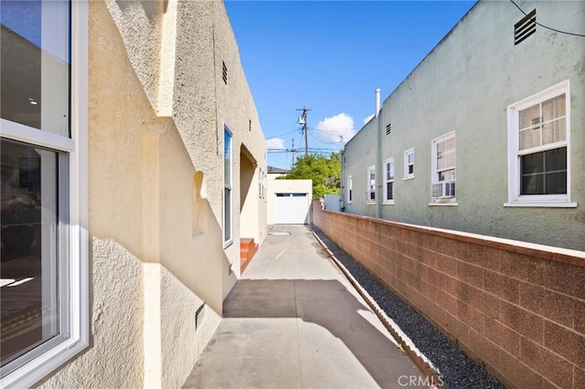 view of property exterior with a detached garage, concrete driveway, stucco siding, and fence