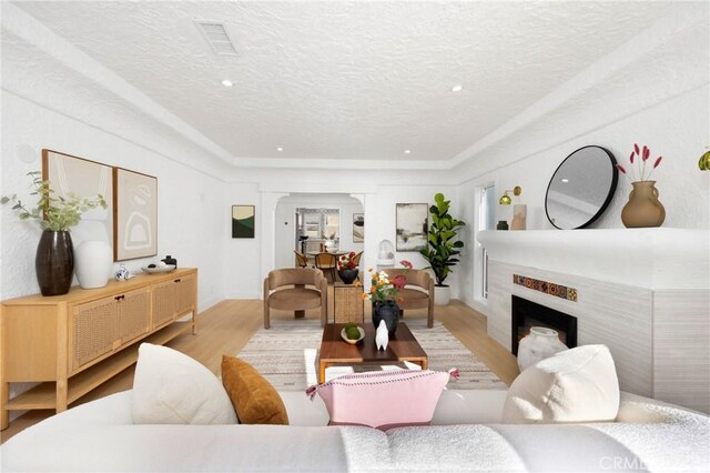 living area with visible vents, baseboards, a textured ceiling, a fireplace, and light wood finished floors