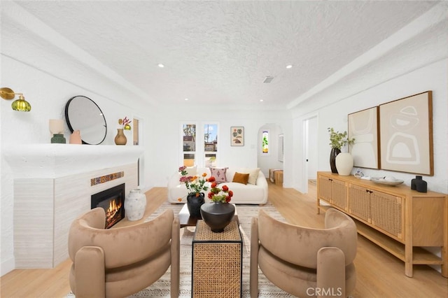 living room featuring a textured ceiling, wood finished floors, a glass covered fireplace, and recessed lighting
