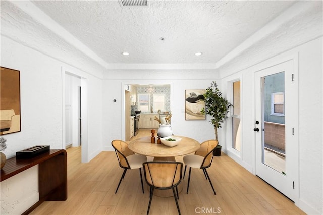 dining room with light wood-style floors, a textured ceiling, french doors, and visible vents