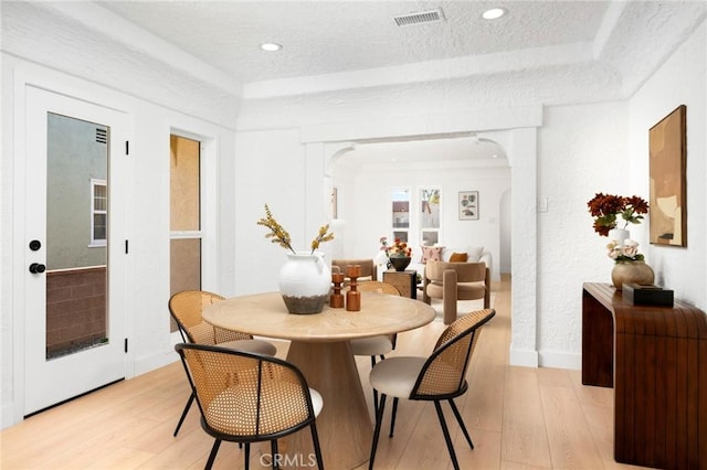 dining room featuring light wood-type flooring, arched walkways, visible vents, a raised ceiling, and baseboards