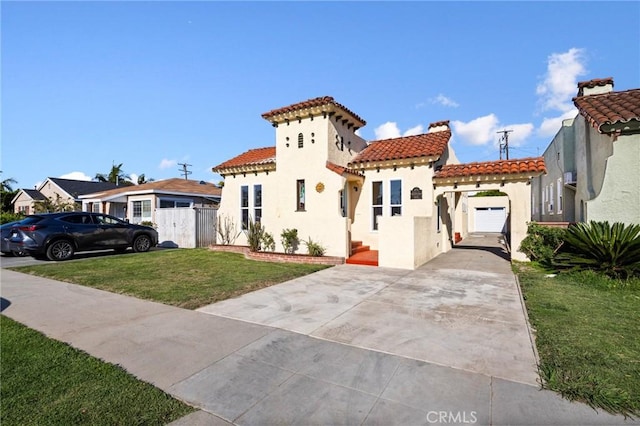 mediterranean / spanish-style home featuring stucco siding, driveway, a front lawn, a tile roof, and fence