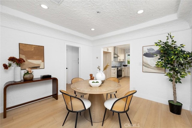 dining space with a raised ceiling, a textured ceiling, and light wood finished floors