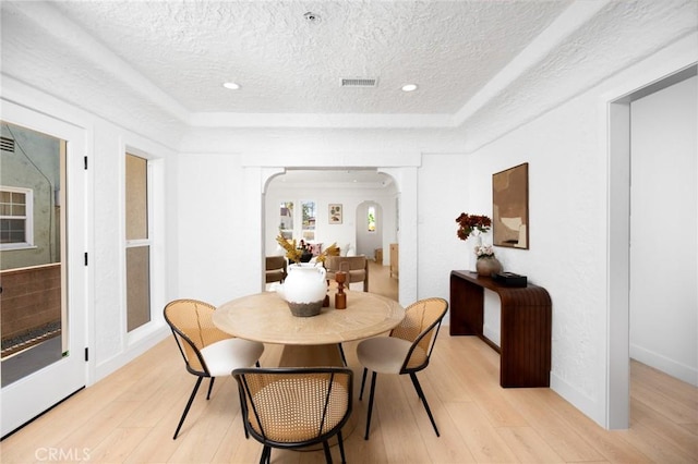 dining area with arched walkways, light wood finished floors, visible vents, and a textured ceiling