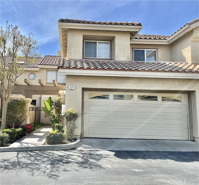 view of front facade with a tiled roof, a garage, fence, stucco siding, and driveway
