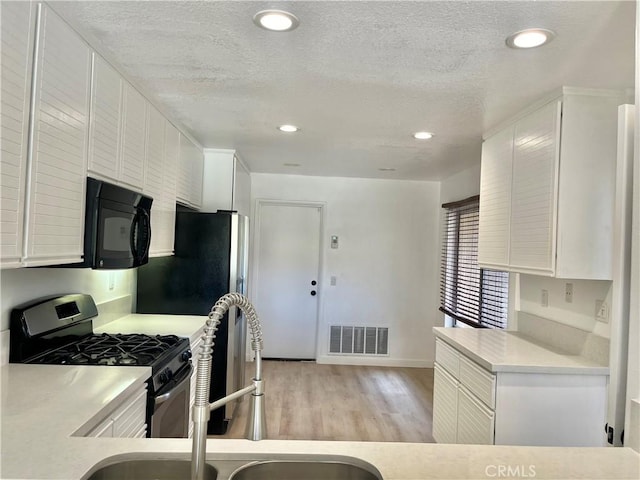kitchen with white cabinets, light wood-style floors, appliances with stainless steel finishes, and visible vents