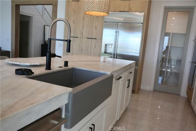 kitchen with light stone countertops, a sink, built in refrigerator, light tile patterned floors, and white cabinets