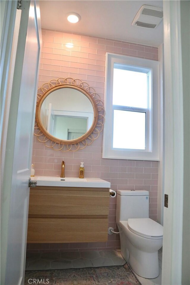 half bath featuring vanity, toilet, tile patterned floors, tile walls, and visible vents
