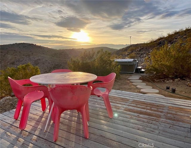 deck at dusk with a mountain view and outdoor dining space