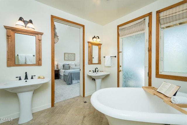 ensuite bathroom with a freestanding tub, baseboards, and a sink