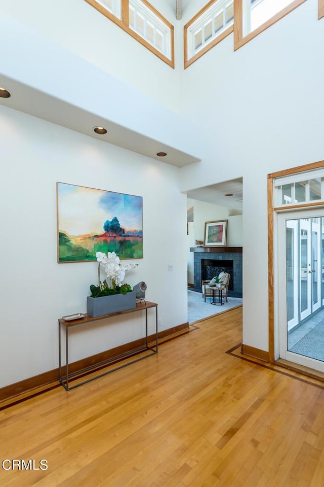entrance foyer featuring light wood-style floors, baseboards, a towering ceiling, and a fireplace