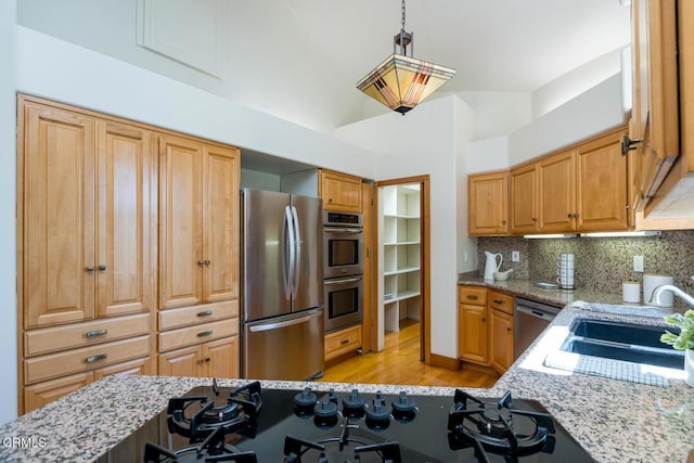 kitchen with appliances with stainless steel finishes, light wood-type flooring, light stone countertops, and a sink