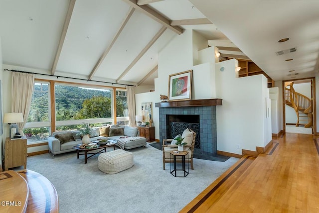 living area featuring high vaulted ceiling, beam ceiling, stairs, a tiled fireplace, and baseboards