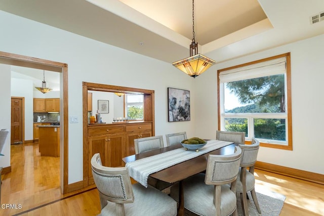 dining room with light wood-style flooring, baseboards, and a raised ceiling