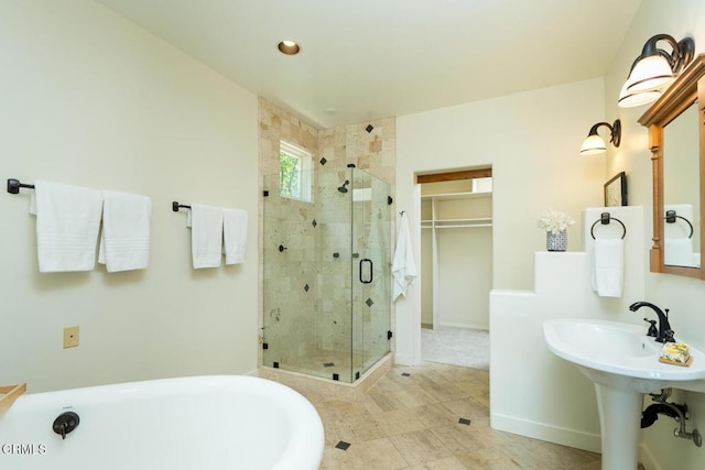full bathroom with a shower stall, a soaking tub, baseboards, a walk in closet, and a sink