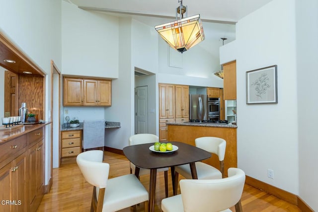 dining space with light wood-style floors, high vaulted ceiling, and baseboards