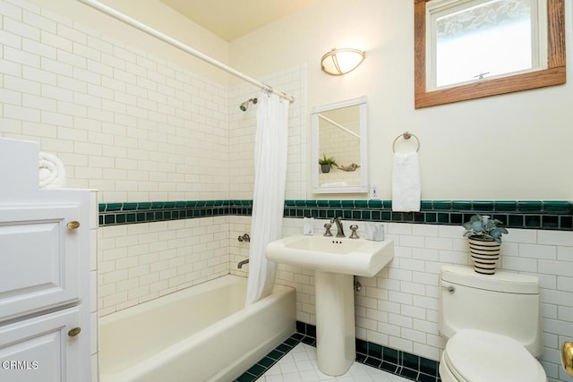 bathroom featuring tile walls, shower / bath combo with shower curtain, toilet, tile patterned floors, and wainscoting