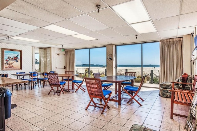 dining area with expansive windows, a paneled ceiling, and a water view