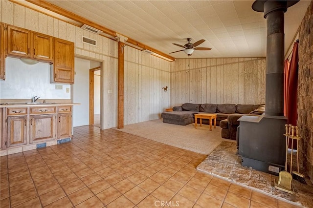 living area featuring a wood stove, wooden walls, visible vents, and ceiling fan