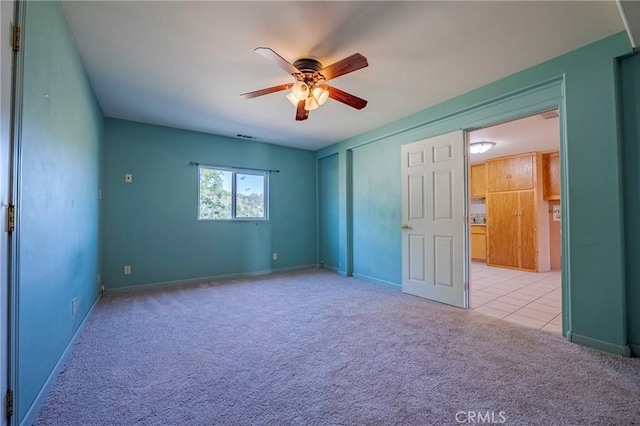 empty room featuring a ceiling fan, visible vents, carpet floors, tile patterned floors, and baseboards