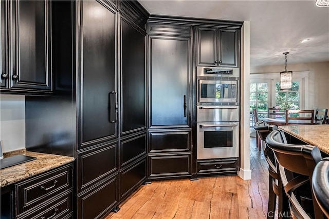 kitchen with light wood-type flooring, dark cabinetry, light stone counters, and stainless steel appliances