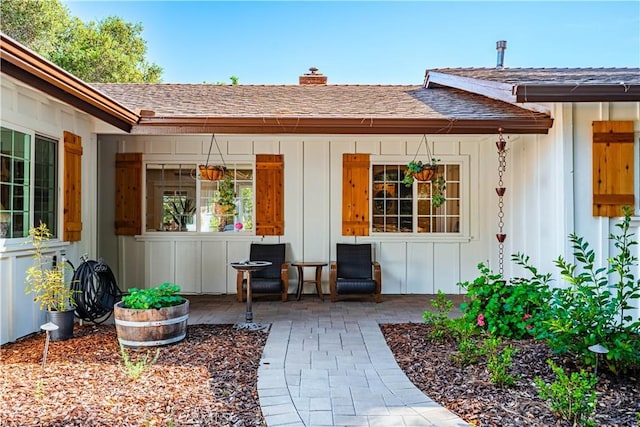 entrance to property with board and batten siding, a shingled roof, a patio, and a chimney