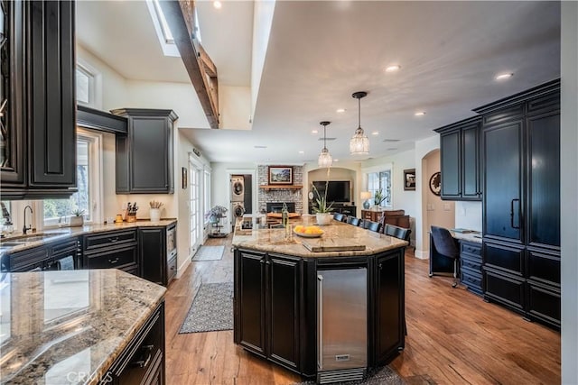 kitchen with dark cabinets, light stone counters, open floor plan, light wood-style floors, and a sink