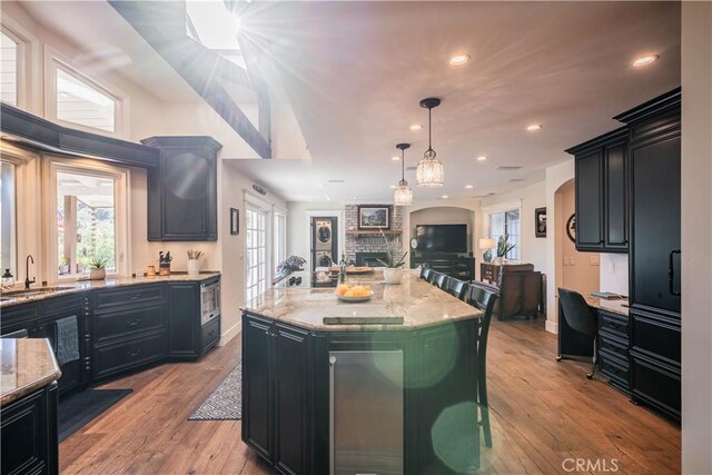 kitchen with a sink, open floor plan, dark cabinetry, and light stone countertops