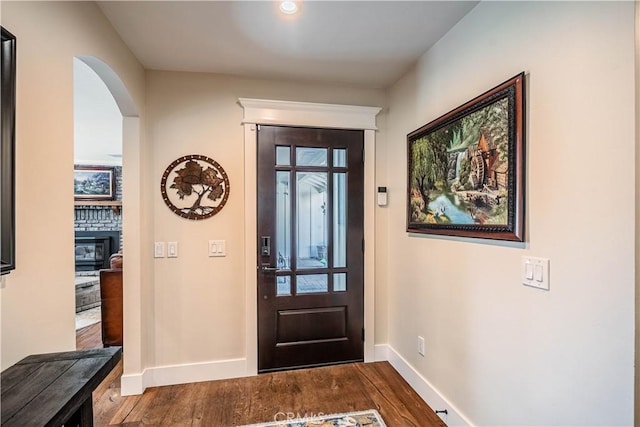 foyer with a glass covered fireplace, arched walkways, dark wood-style flooring, and baseboards