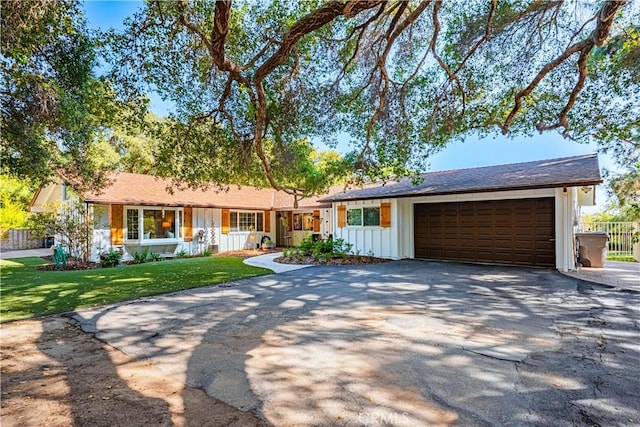 ranch-style house featuring board and batten siding, a front yard, an attached garage, and driveway